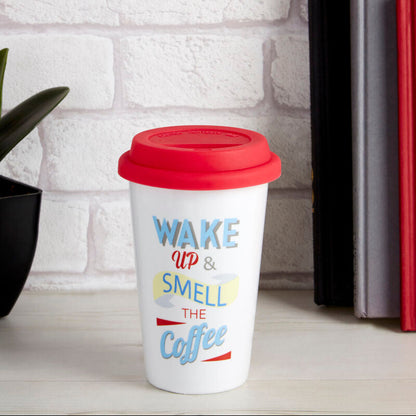White travel mug with red lid and colorful text on a white surface with books and flowers in the background.