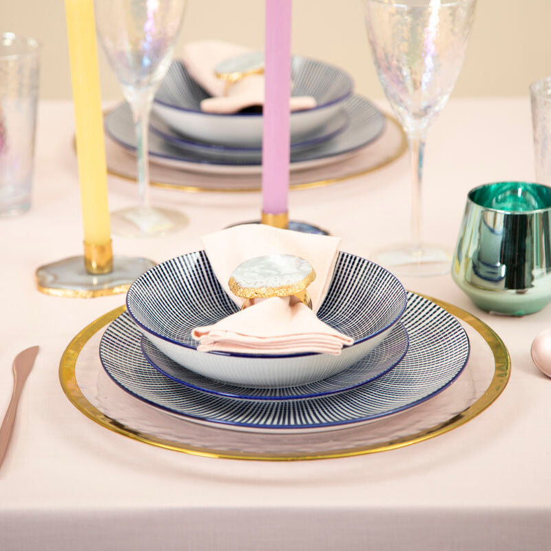 Elegant table setting with blue and gold plates, silverware, and candles on a white table.
