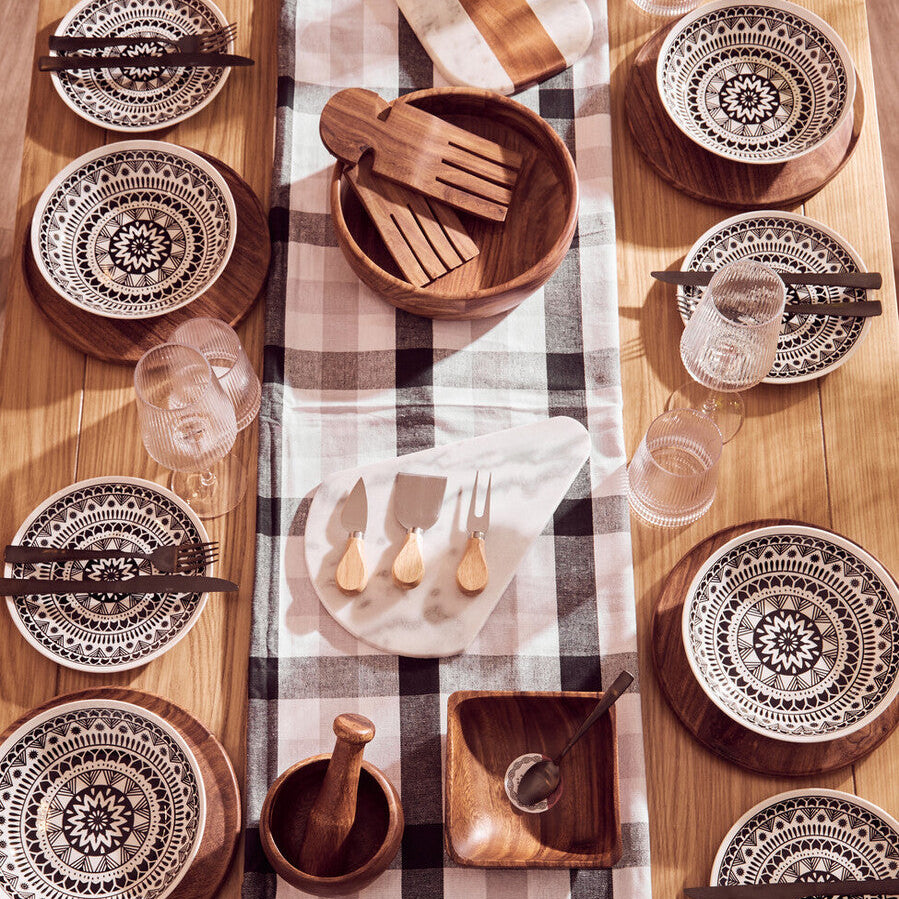 Dining table setting with decorative plates, wooden cutlery, and a checkered tablecloth.