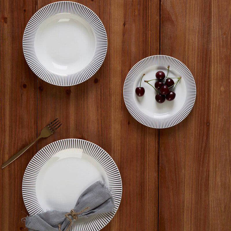 Three white plates with decorative edges on a wooden surface, one with a gray napkin and another with cherries.