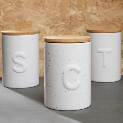 Three white ceramic canisters with wooden lids on a wooden background
