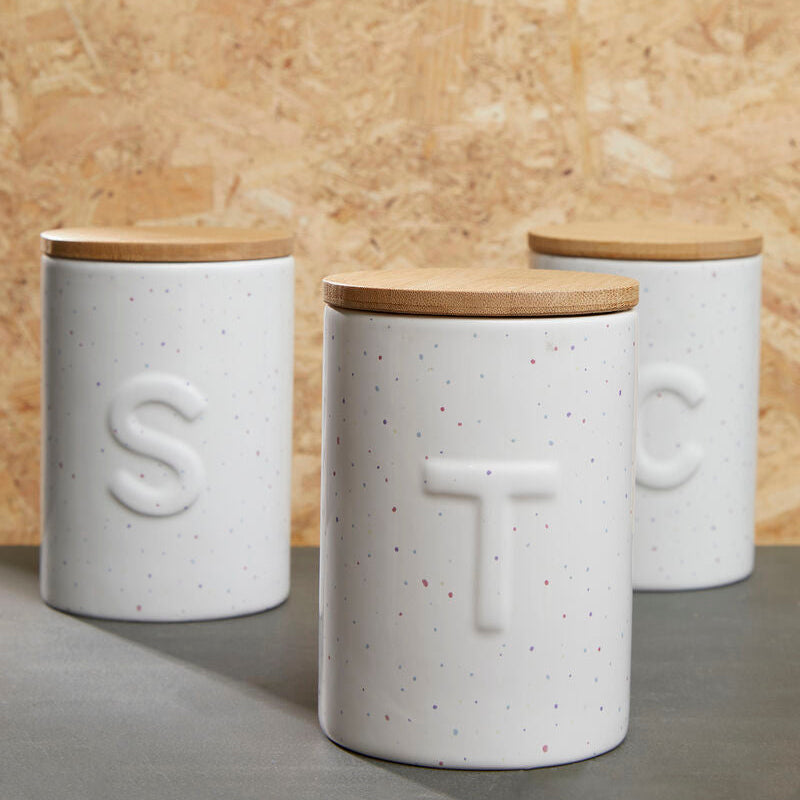 Three white canisters with wooden lids on a gray surface against a beige wall.