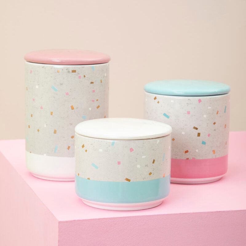 Three pastel-colored ceramic jars with colorful confetti pattern on a pink surface.