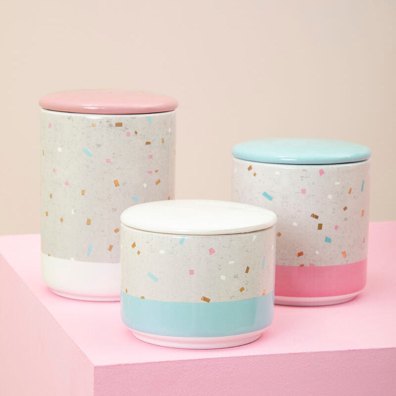 Three pastel-colored canisters with colorful confetti pattern on a pink surface.