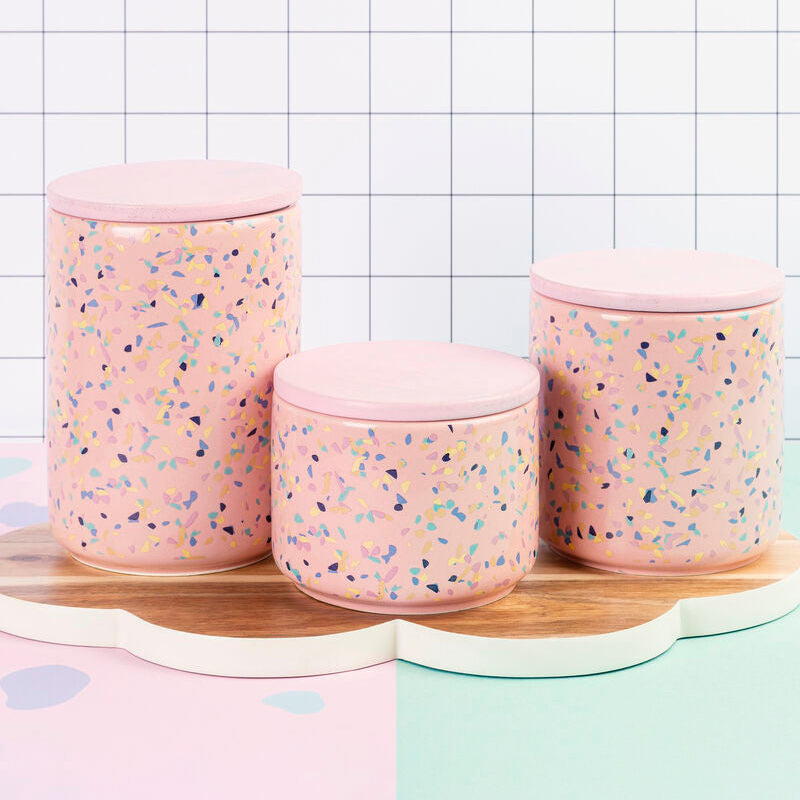 Three pink textured storage jars on a wooden surface with a white grid background