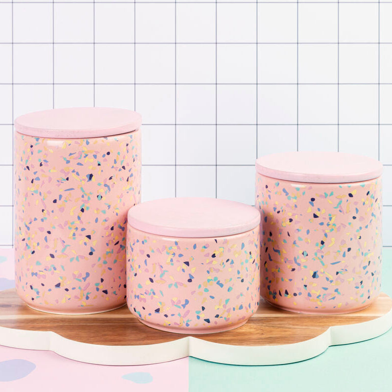 Set of three pink textured jars with a wooden tray on a checkered background