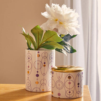Two patterned vases with a white flower on a wooden surface.