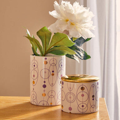 Two patterned vases with a white flower on a wooden surface.