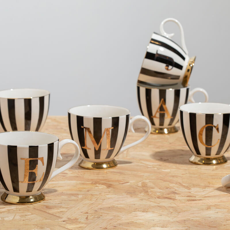 Set of black and white striped mugs with gold lettering on a wooden surface.