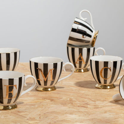 Set of black and white striped mugs with gold lettering on a wooden surface.