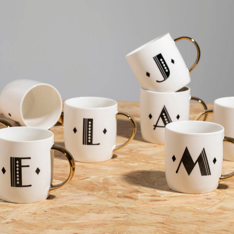 Set of white mugs with black letter designs on a wooden surface