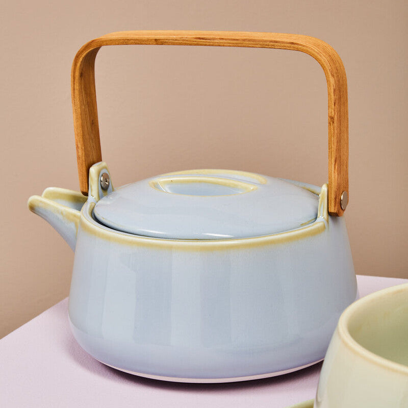 Ceramic teapot with wooden handle on a pink surface, with a beige background