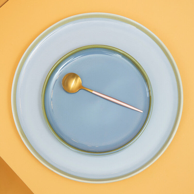 Stack of ceramic plates with a gold spoon on a yellow surface