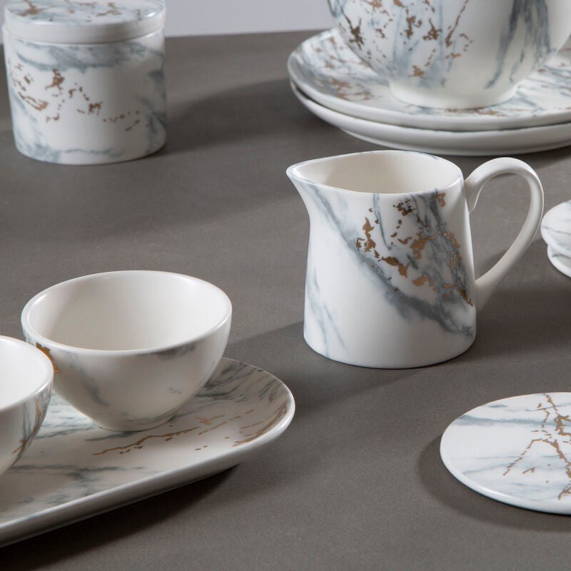 Marble-patterned ceramic tableware including cups, plates, and coasters on a gray surface.