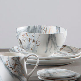 Set of marble-patterned ceramic tea set on a gray surface with a light gray background