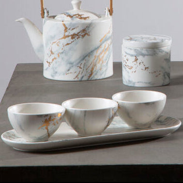 Set of marble-patterned ceramic tea set on a gray surface with a light gray background