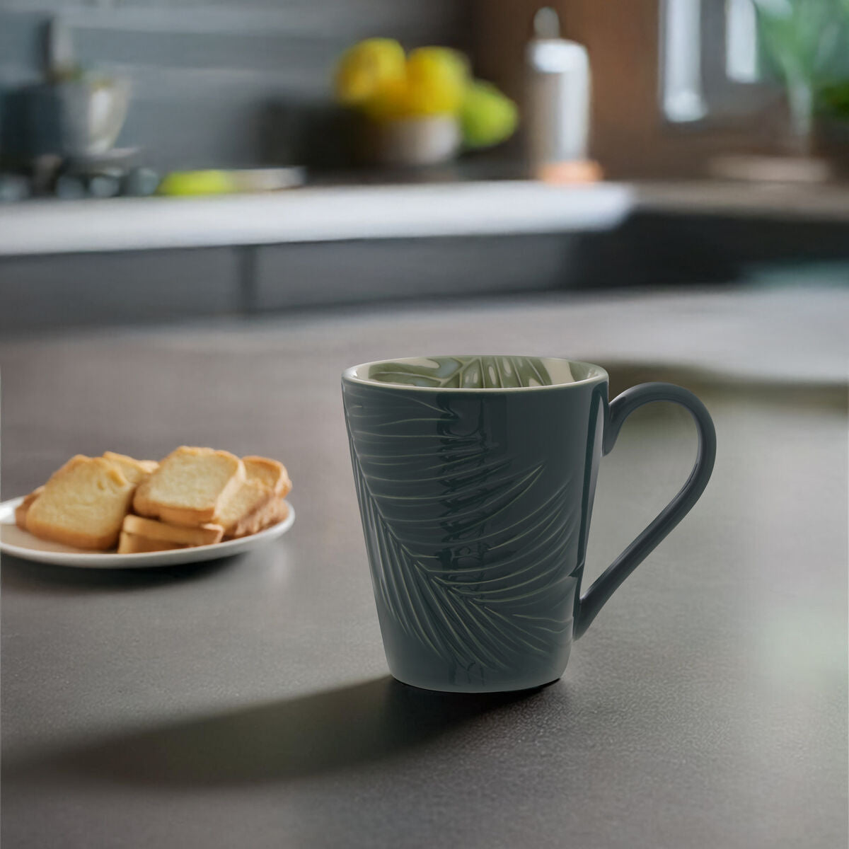 Green mug with leaf pattern on a kitchen counter with toast and fruit in the background