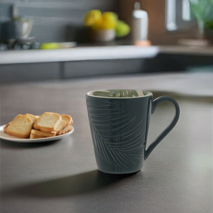 Green mug with leaf pattern on a kitchen counter with toast and fruit in the background
