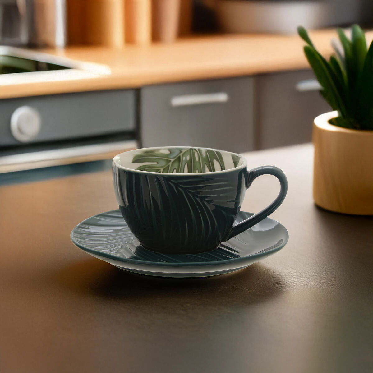 Green ceramic cup and saucer on a kitchen counter with a plant in the background