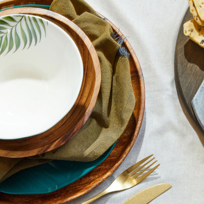 Dining setup with wooden plates, green napkin, and gold cutlery on a light gray surface.