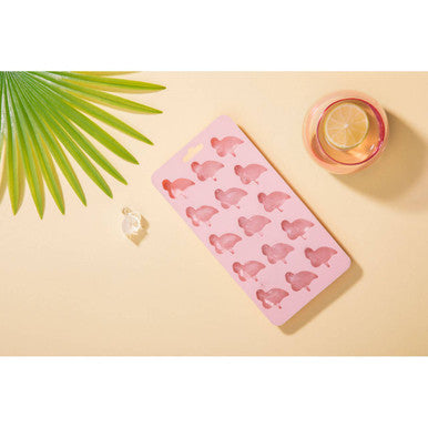 Pink silicone ice cube tray with turtle molds on a beige surface with a glass of water and green leaf decoration.
