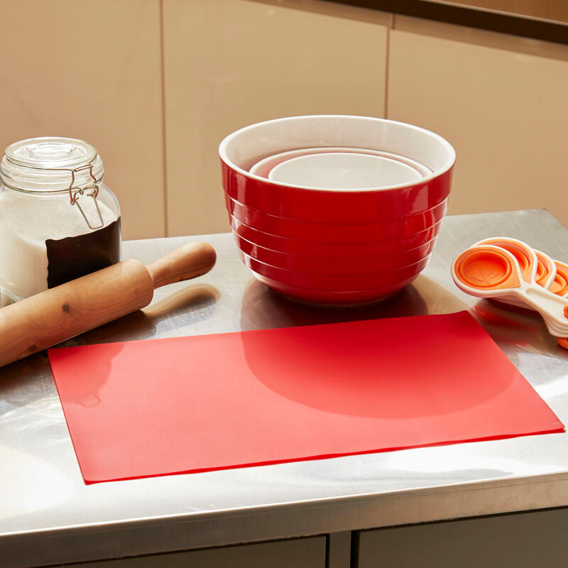 Red mixing bowl, cutting board, rolling pin, and jars on a kitchen counter.