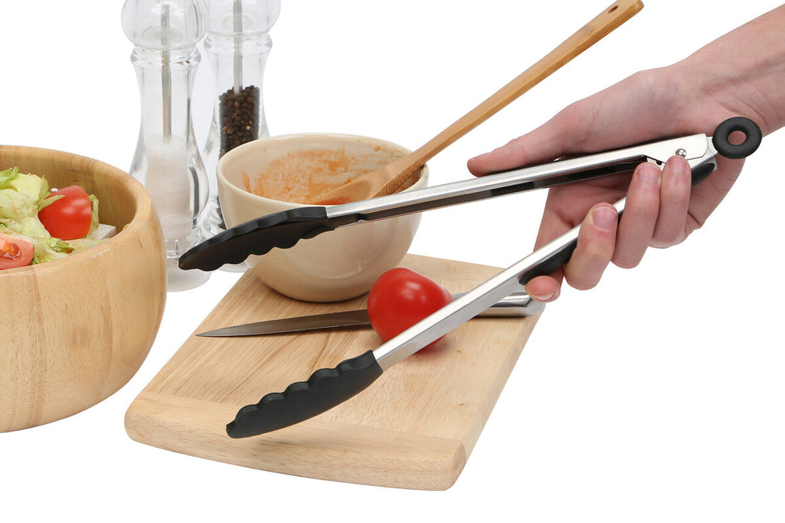 Person using tongs on a wooden cutting board with a bowl of salad and tomatoes in the background.