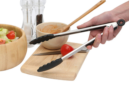 Person using tongs on a wooden cutting board with a bowl of salad and tomatoes in the background.