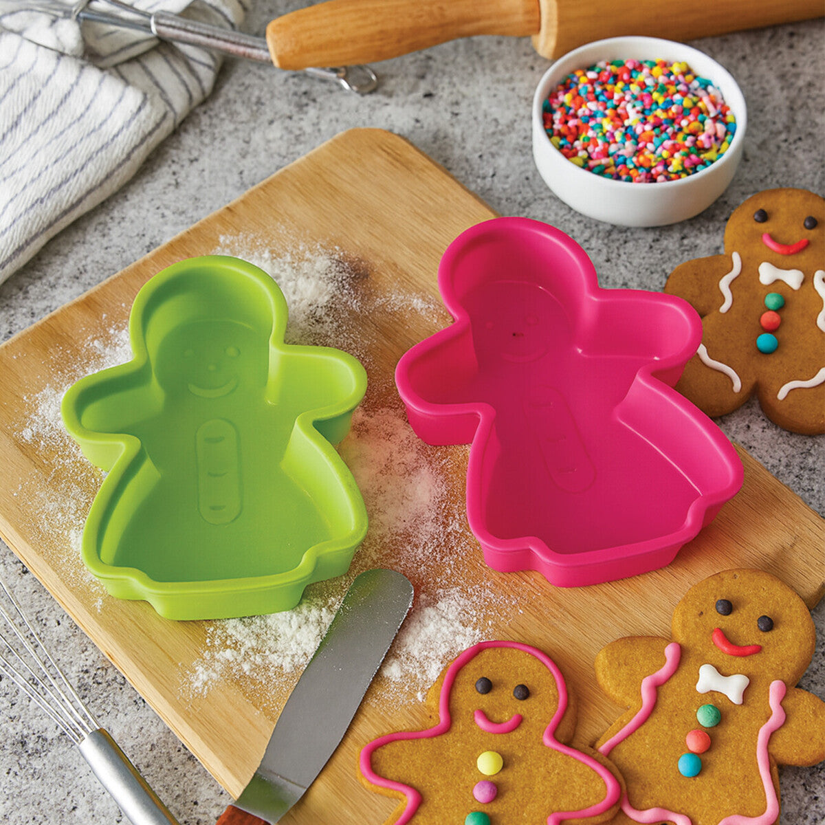 Gingerbread cookie cutters and decorated cookies on a wooden board with sprinkles.
