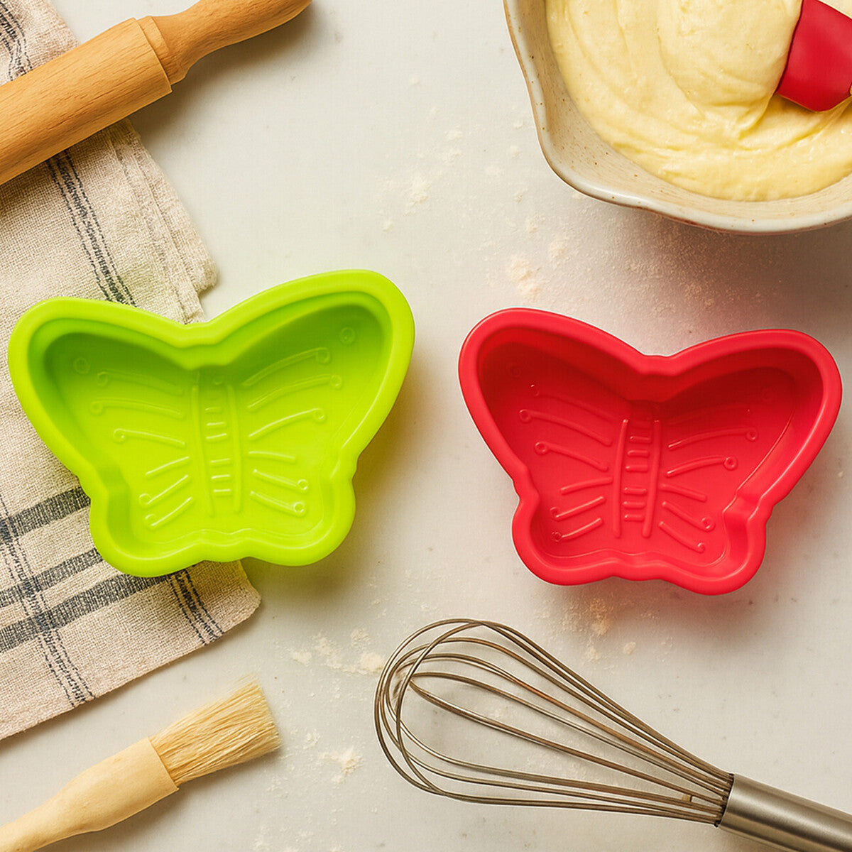 Two butterfly-shaped silicone molds on a kitchen counter with a whisk and baking tools.