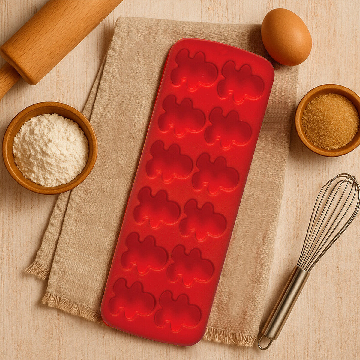 Red silicone mold with bear shapes on a wooden surface with baking ingredients and tools.