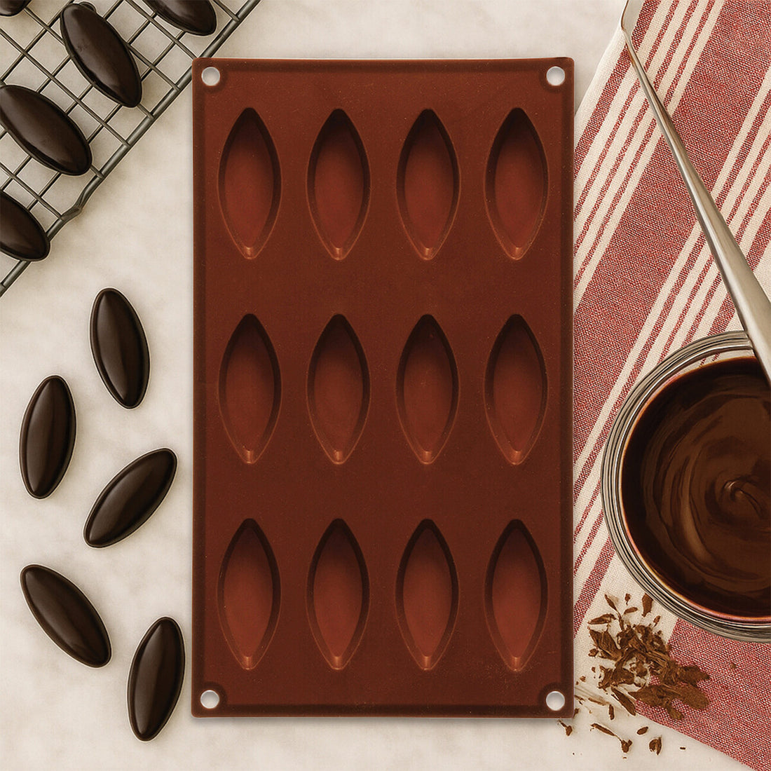 Silicone mold with chocolate shapes on a marble surface with a jar of chocolate and a striped cloth.