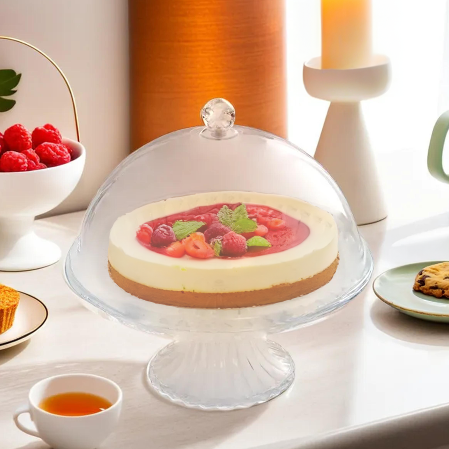 Cheesecake on a clear plastic cake stand with berries, surrounded by tea and cookies.