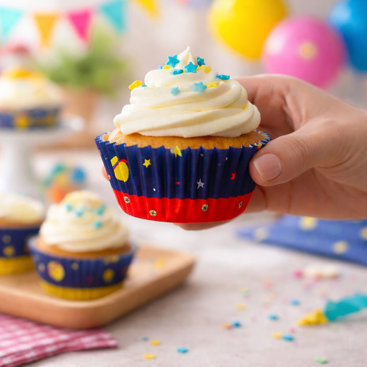 Hand holding a cupcake with star-themed wrapper on a festive background