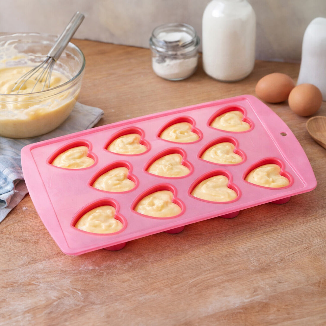 Pink heart-shaped silicone mold with batter on a wooden table