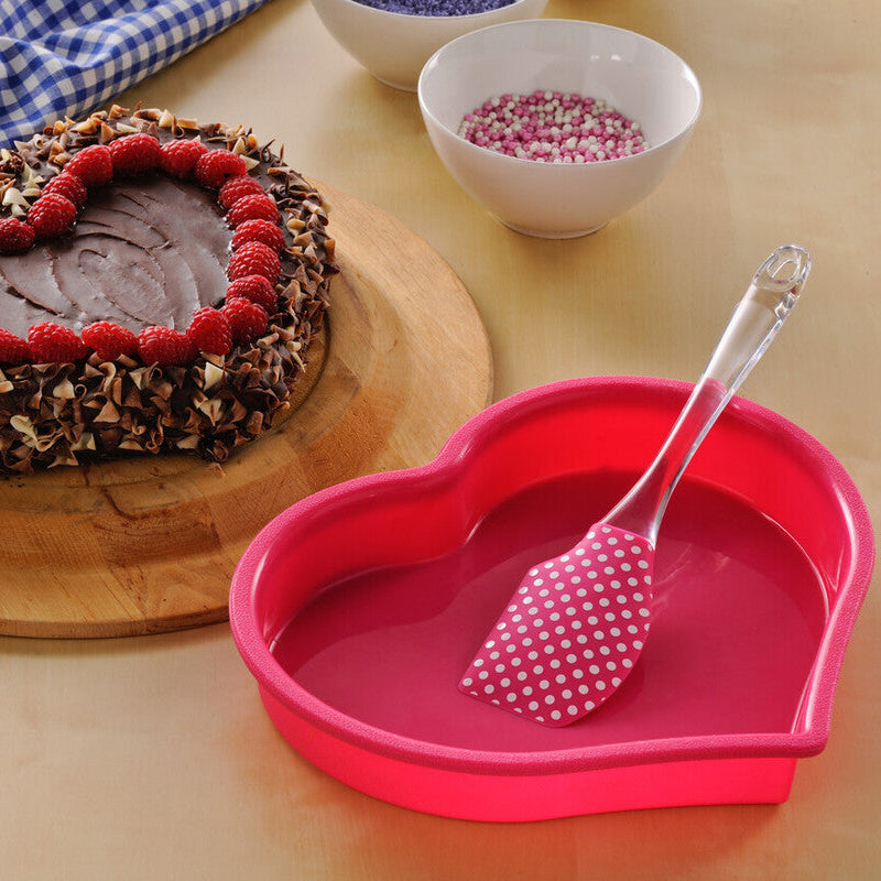 Heart-shaped cake with raspberries on a wooden board, surrounded by bowls of berries and a pink heart-shaped dish with a spoon.