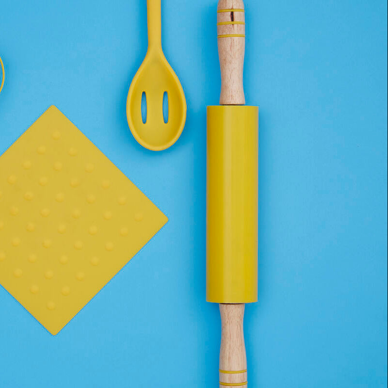 Yellow kitchen utensils including a whisk, spatula, cutting board, and rolling pin on a blue background
