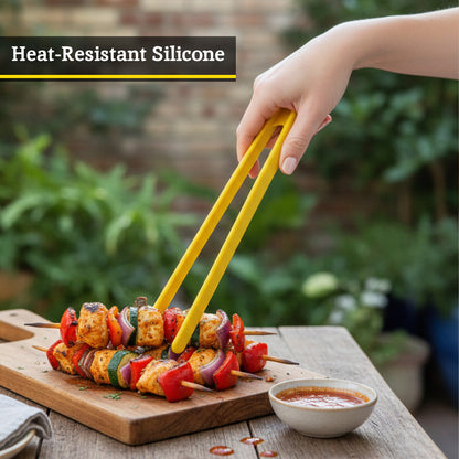 Person using yellow silicone tongs to handle skewered vegetables on a wooden board with a blurred outdoor background.