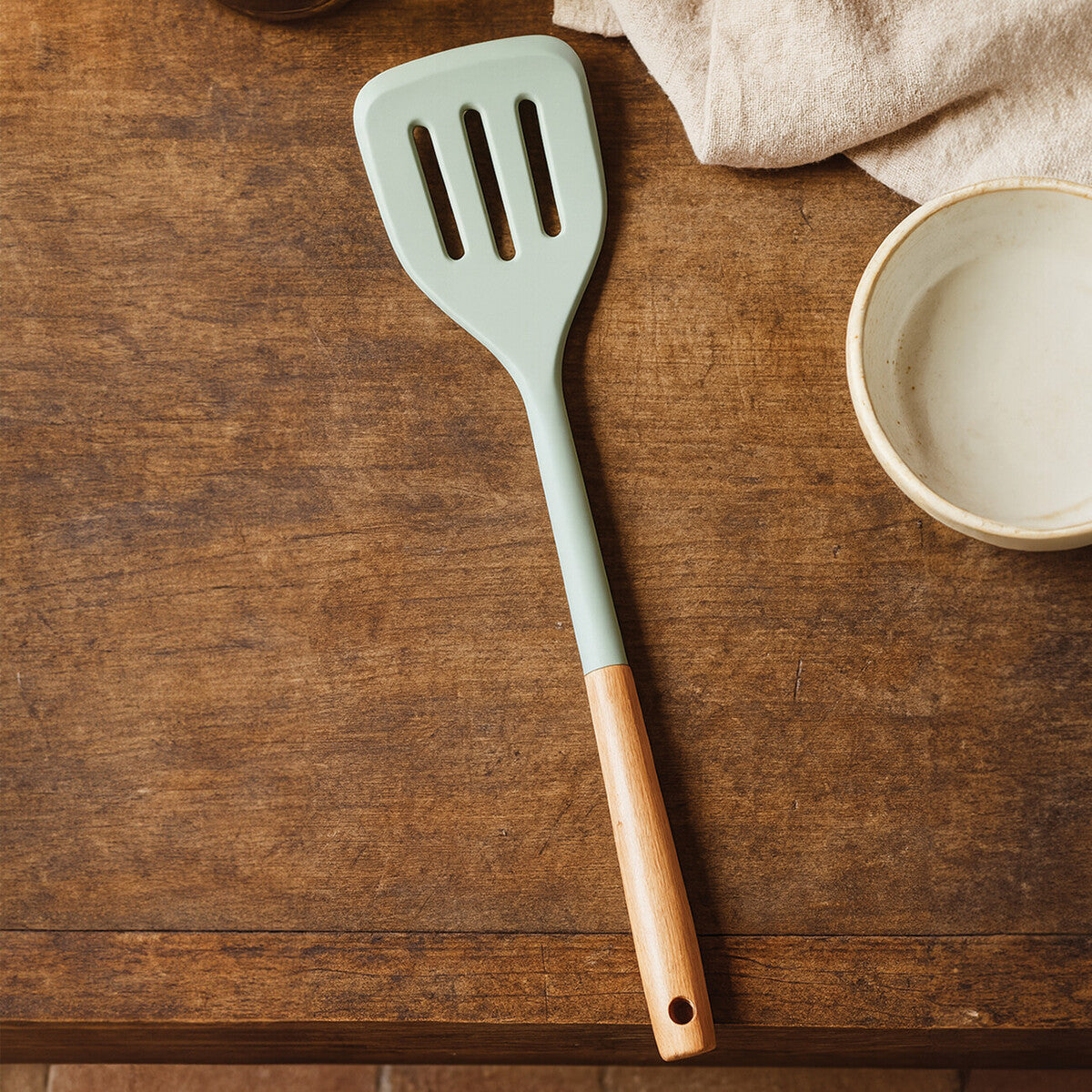 Green slotted spatula with wooden handle on a wooden surface