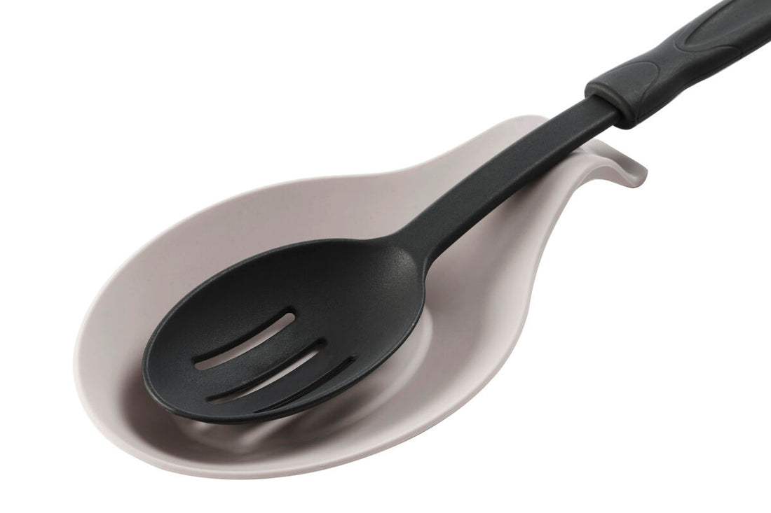 Black slotted spoon on a metallic ladle against a white background