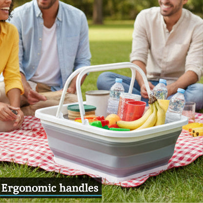 People sitting on a picnic blanket with a large picnic basket filled with food and drinks.