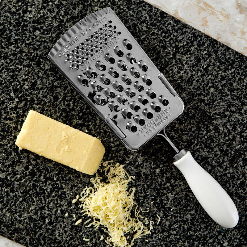 Metal grater with a block of cheese and grated cheese on a dark surface