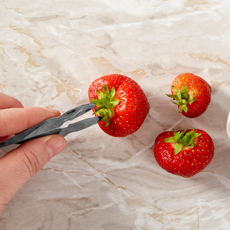 Strawberries being picked up with tongs on a marble surface
