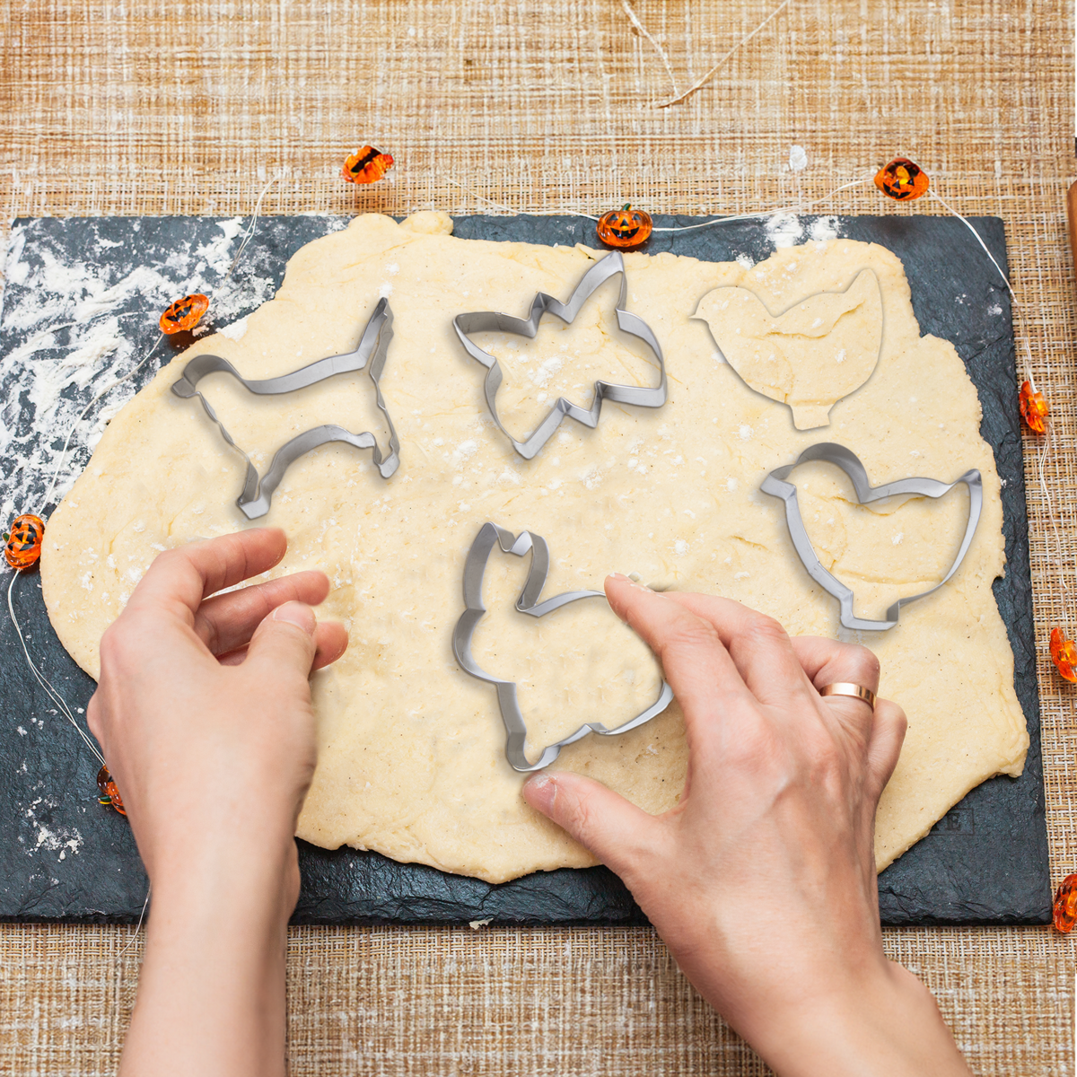 Hands arranging cookie dough with Halloween-themed cutters on a slate surface.