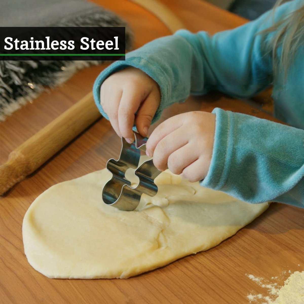 Child using a stainless steel cookie cutter on dough with a wooden rolling pin in the background.