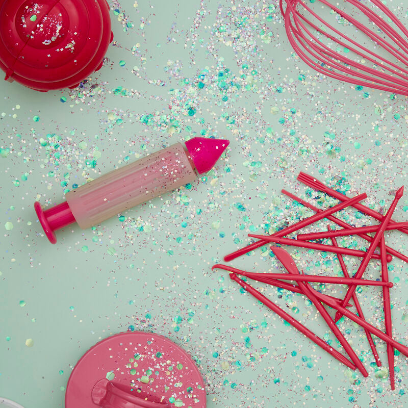Pink baking tools and utensils on a light green surface with sprinkles.