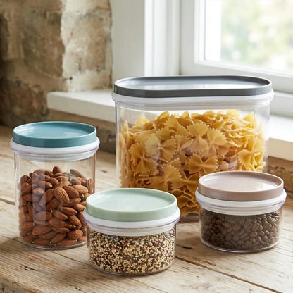 Set of four glass storage jars with lids on a wooden surface, containing various foods.