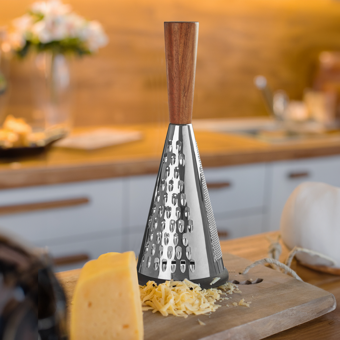 Cheese grater with wooden handle on a kitchen counter with cheese and flowers in the background