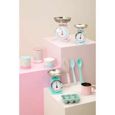 Kitchen scales, cups, and utensils on a pink and white background