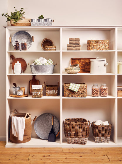 White shelving unit with various baskets and decorative items on a wooden floor.